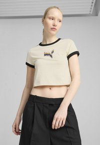Beskåret beige t-shirt med sort kant, der har et flerfarvet stribet logo. Stoffet har en glat tekstur og er designet til afslappet brug.