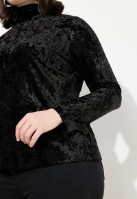 Schwarzes Samtoberteil mit hohem Kragen und langen Ärmeln, das eine strukturierte Glanzoberfläche und eine taillierte Silhouette aufweist. Einfaches Design, keine sichtbaren Beschläge.