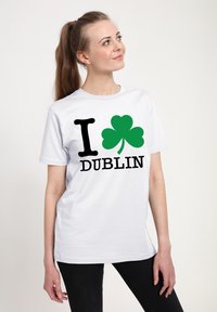 Bílý bavlněný tričko s černým nápisem "I DUBLIN" a zeleným motivem trojlístku. Krátké rukávy, výstřih do véčka, volný střih.