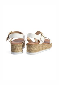 Sandales blanches à talon en jute tressé, avec une bride de cheville ajustable en métal doré et un pied en cuir lisse couleur tan.