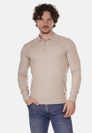 Polo shirt beige a maniche lunghe con colletto, tre bottoni, polsini a coste e orlo a coste. Indossato con jeans in denim blu.