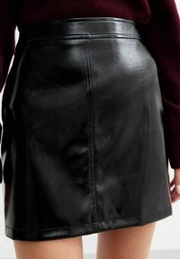Falda corta de cuero negro con una textura suave, de cintura alta y con costuras visibles a lo largo de las costuras. Sin otras características notables.