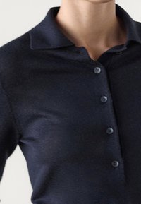 Tummansininen polo-paita pehmeästä kankaasta, jossa on kaulus ja kolmonen nappeja sisältävä nappilista, esittelee sileää pintaa.