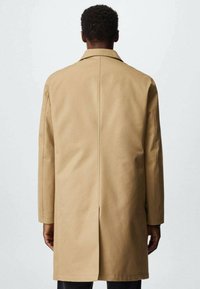 Beige trenchcoat met een ontspannen pasvorm, voorzien van een achtersplit, een brede kraag en lange mouwen, gemaakt van een gladde, gestructureerde stof.