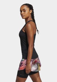 Zwarte mouwloze sporttop met een kleurrijke, gemusterde rokoverlay. Het materiaal lijkt rekbaar; de zwarte shorts eronder zijn aansluitend.