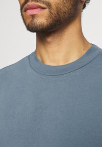 T-shirt blu in cotone a girocollo con una texture morbida. Presenta un collo a costine e dettagli di cucitura minimi. Colore chiaro e uniforme.