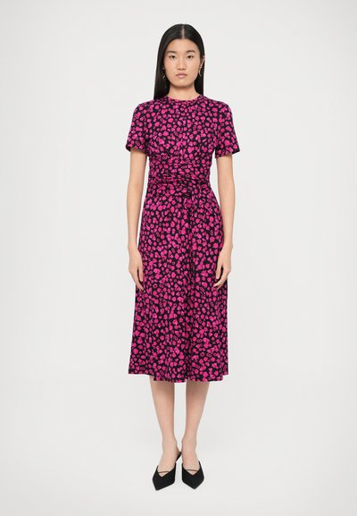 Kurzärmeliges, knielanges Kleid in schwarzem und rosa Blumenmuster, mit geraffter Taille und einer Bindedetail, kombiniert mit schwarzen High Heels.