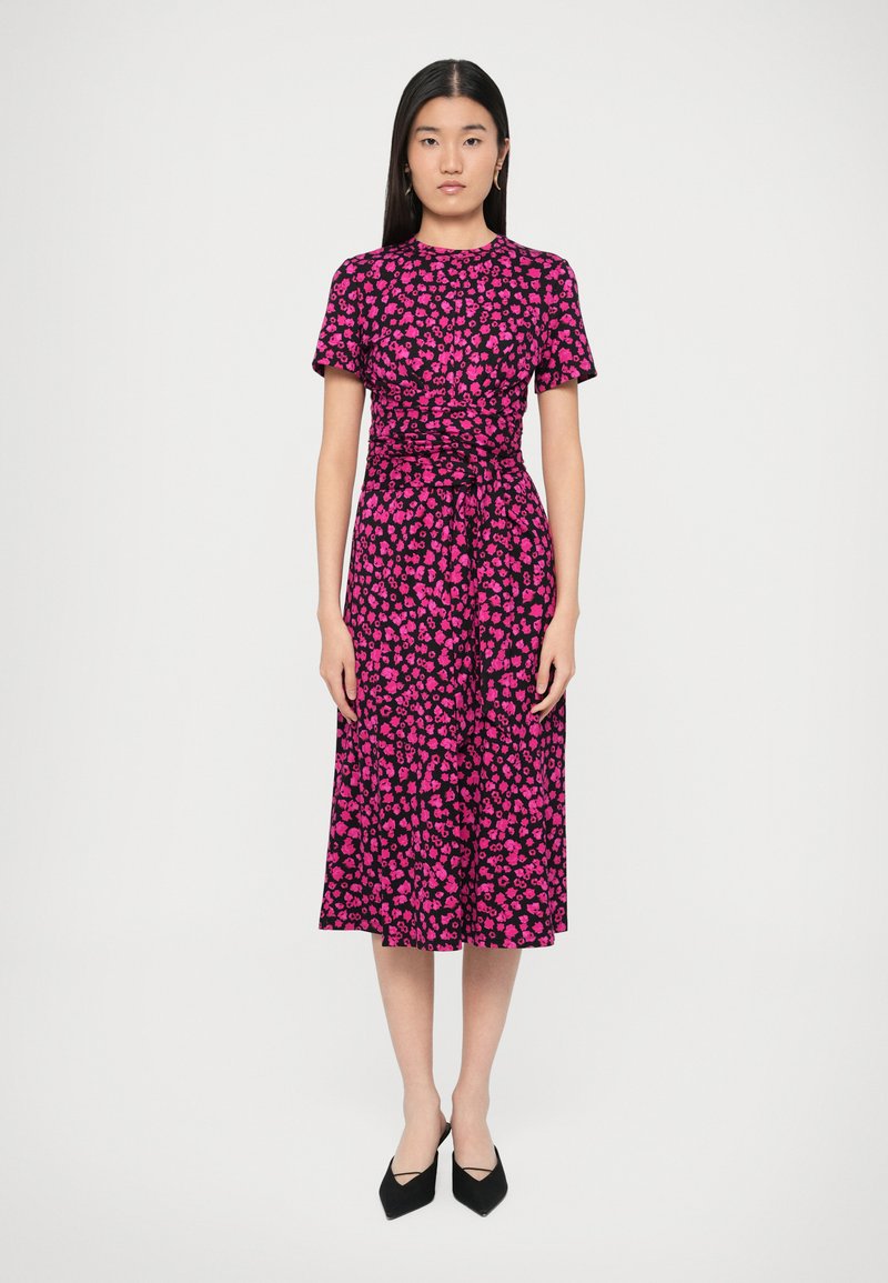 Sukienka z krótkim rękawem, o długości do kolan, w czarno-różowy kwiatowy wzór, z marszczoną talią i wiązaniem, zestawiona z czarnymi szpilkami.