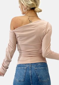Rosa off-shoulder topp med långa ärmar, med rynkade detaljer, tillverkad av ett elastiskt tyg. Kombineras med blå denimjeans.