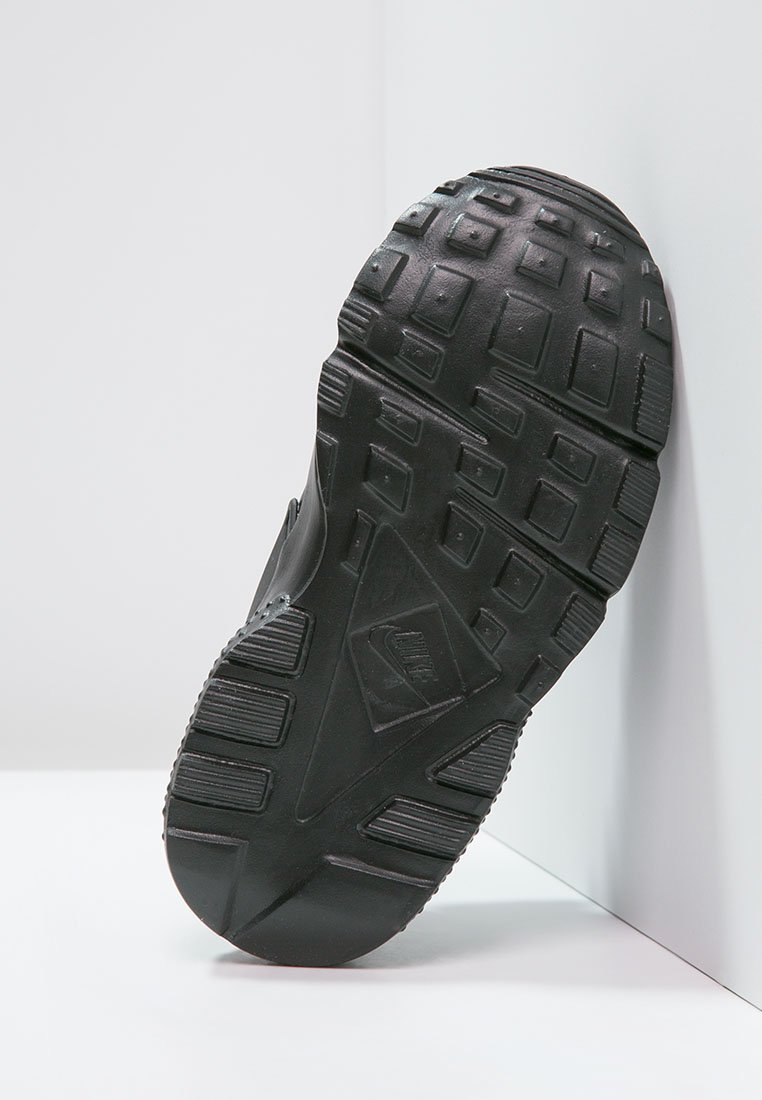 Suela de zapatilla de goma negra con profundos surcos, que presenta patrones rectangulares y cuadrados. Logotipo grabado en el centro. Superficie duradera y texturizada.