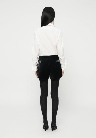 Fekete bársony sort virágmintás hímzéssel a zsebeken, fehér, hosszú ujjú inggel és fekete harisnyával párosítva. A lábbelin kisméretű sarok található.