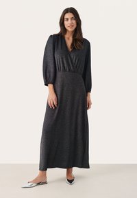 Svart långärmad omslagsklänning med en texturerad, skimrande tyg. Har en djup V-ringning och en figurnära midja. Bärs med silverfärgade slingback-skor.