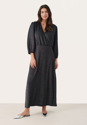 Vestido negro de manga larga y corte envolvente con una tela texturizada y brillante. Presenta un escote en V profundo y una cintura ajustada. Combinado con unas bailarinas plateadas.