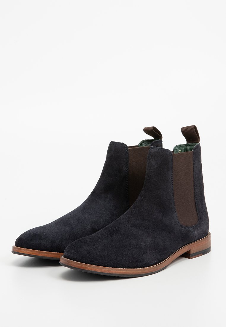 Navyblaue Wildleder Chelsea Boots mit braunen elastischen Seitenpaneelen und einer hellbraunen Holzsohle. Mit einer Schlaufe für einfaches Anziehen.