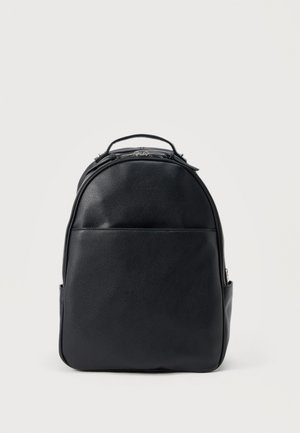Sac à dos en cuir noir avec poignée supérieure, poche avant et compartiment principal zippé sur fond clair uni.