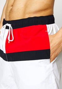 Costumi da bagno da uomo con blocchi di colore orizzontali in rosso, nero e bianco, cintura elastica e coulisse, tessuto dalla trama liscia.