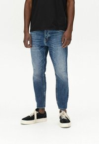 Jeans din denim albastru, cu o croială subțire și detalii decolorate, asortați cu adidași din suede negri și un tricou negru. Un design simplu și casual.