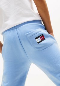 Pantalones de chándal de algodón azul claro con un bolsillo trasero que presenta un parche de logotipo multicolor. Textura suave, cinturilla elástica y corte casual.