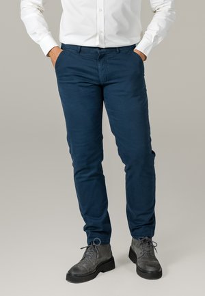 Navy blue chinos made of cotton with a slim fit and side pockets, paired with gray lace-up boots and a white button-up shirt.
