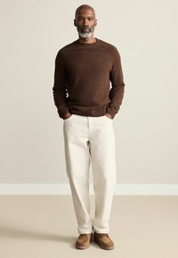 Brauner gestrickter Pullover mit gerippten Bündchen und Saum, kombiniert mit off-white lässigen Hosen und braunen Wildlederschuhen. Einfaches, strukturiertes Design.