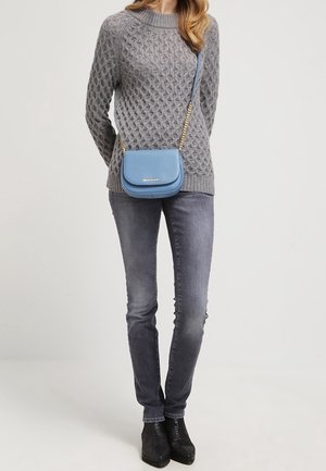 Šedý pletený svetr s texturovaným vzorem, kombinovaný se šedými džíny a černými kotníkovými botami. Malá modrá crossbody taška má zlatý řetěz.