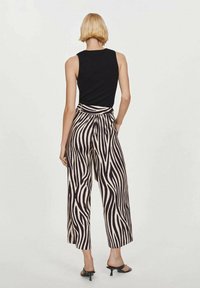 Haut noir sans manches associé à un pantalon large à motif zébré noir et crème, avec une taille haute et un tissu lisse.