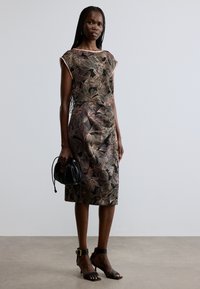 Mustrites lilleline kleit musta, roosa ja kuldse tooniga, lühikeste varrukatega ja põikpealne siluett. Must käekott ja pahkluu rihmaga sandaalid.