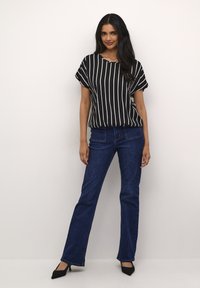 Top a maniche corte a righe bianche e nere, vestibilità comoda, abbinato a jeans a zampa d'elefante blu e scarpe con tacco nere. Design semplice e casual.