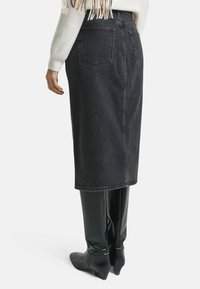 Gonna di jeans neri di lunghezza media con un taglio dritto, due tasche posteriori e un orlo semplice. Indossata con stivali neri lucidi fino al ginocchio.