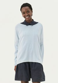 Himmelblauer Pullover mit entspannter Passform, langen Ärmeln und Rundhalsausschnitt, über einem dunkelblauen Kragenkleid getragen.