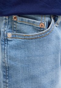 Jeans in denim azzurro chiaro con una superficie testurizzata, caratterizzati da rivetti in rame sulle tasche anteriori e cuciture a contrasto.