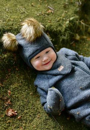 Grau melierter Fleece-Overall und Mütze mit pelzverzierten Ohren. Liegt auf moosigem Boden und verfügt über einen seitlichen Reißverschluss sowie eine strapazierfähige Stoffstruktur.