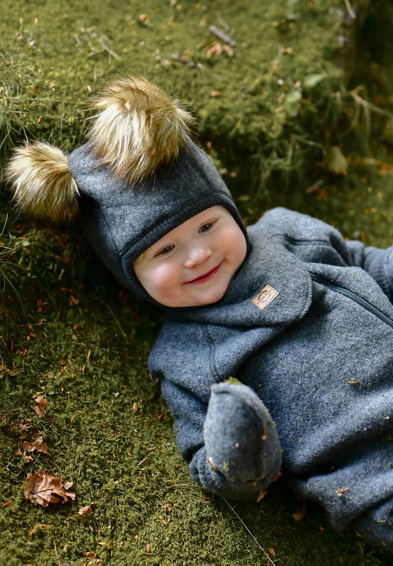 Sivý flísový overal a čiapka s chlpatými uškami. Položené na machovej zemi, s bočným zipsom a odolnou textúrou látky.