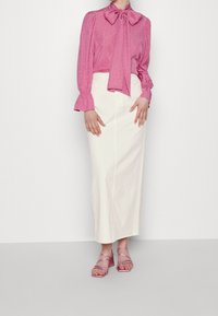 Rosa långärmad blus med knytband och strukturerade prickar, kombinerad med en vit knä längd kjol och genomskinliga rosa höga klackar.