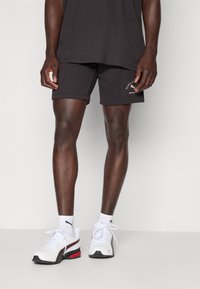 Sorte treningsshorts med en avslappet passform, parret med hvite joggesko med røde detaljer. Antrekket suppleres med en løs mørk t-skjorte.