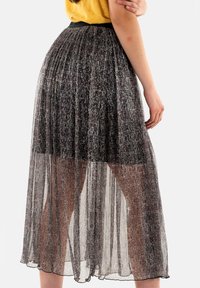 Jupe longue plissée en matériau noir semi-transparent avec des accents métalliques, dotée d'une taille ajustée et d'un design en couches, affichant des textures douces.