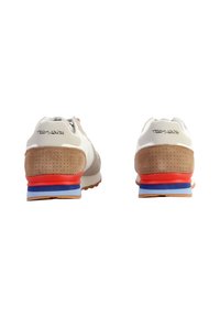 Zapatillas deportivas blancas con detalles en ante beige, media suela roja y detalles azules, que presentan un logo en la parte trasera y una textura perforada en el talón.