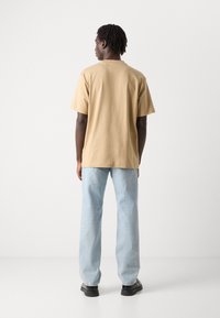 Beige bomull t-skjorte med en avslappet passform, korte ermer og rund hals, kombinert med lyseblå denim jeans og svarte sko.