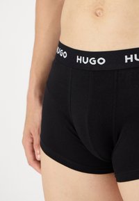 Boxer shorts in cotone nero con una morbida vita elastica su cui è presente il logo "HUGO" in bianco. Il design è aderente, caratterizzato da una texture liscia e cuciture minime.