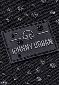 Czarna, teksturowana tkanina z kroplami wody. Posiada wypukłą czarną naszywkę z logo oznaczoną "JOHNNY URBAN" w szarym kolorze. Trwała i wodoodporna konstrukcja.