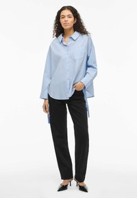 Chemise boutonnée à manches longues de couleur bleu clair avec une poche poitrine, associée à un pantalon noir et des talons noirs à bouts pointus. Design épuré, coupe décontractée.