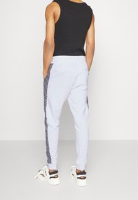 Hellblaue Jogginghosen mit strukturierten schwarzen Seitenstreifen, elastischem Bund und gerippten Knöcheln. Getragen mit einem schwarzen ärmellosen Shirt.