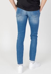 Vaqueros skinny de denim azul con un efecto desgastado, bolsillos traseros con detalles de costura, combinados con zapatillas blancas y calcetines por el tobillo.