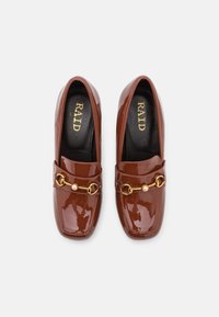 Mocassins en cuir verni marron à bout carré, présentant une chaîne dorée décorative et un accent en perle sur le coup de pied. Marque : RAID.