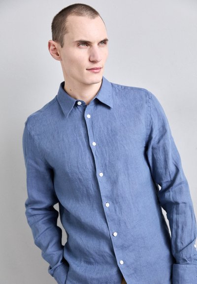 Camisa de lino de manga larga de color azul claro con cuello abotonado, que presenta un corte holgado y botones blancos en la parte delantera y en los puños.