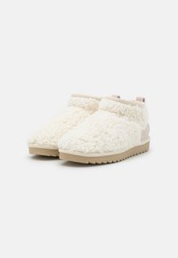 Botas blancas, esponjosas y de altura hasta el tobillo, con una superficie texturizada, acentos beige y una suela de goma con un patrón en zigzag para mayor agarre.