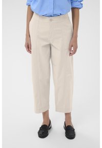Pantalons cropped beige clair avec une coupe droite, dotés de poches latérales et de détails de surpiqûres. Portés avec des mocassins noirs.