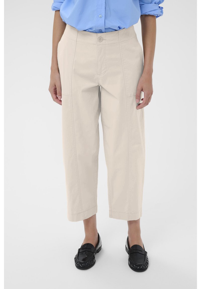 Pantalons cropped beige clair avec une coupe droite, dotés de poches latérales et de détails de surpiqûres. Portés avec des mocassins noirs.