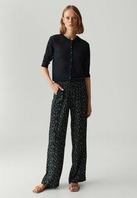 Cardigan tricot navy avec fermeture à bouton, associé à un pantalon à jambes larges avec un motif dans des couleurs sombres, featuring une coupe décontractée et une taille élastique.