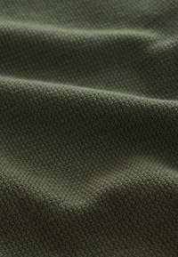 Tela de color verde oliva oscuro con textura y un tejido apretado en zigzag, que muestra contornos suaves en la superficie y sutiles variaciones en el tono.